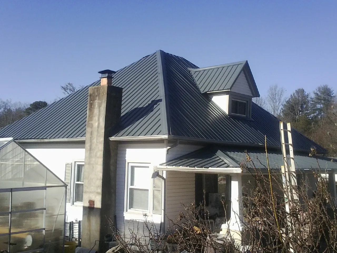 Dark blue standing seam metal roof on a white farmhouse with dormer — Slate & Tile Roof Repair by Roofing Brothers in Glenn