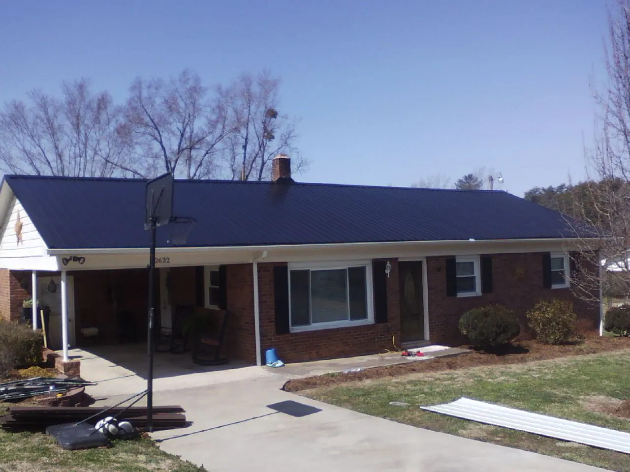Finished dark blue metal roof on a brick ranch with a carport in Glenn