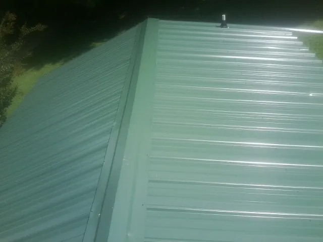 New green metal panels meeting at the ridge of a roof — Flat Roof Repair work by our crew in Glenn