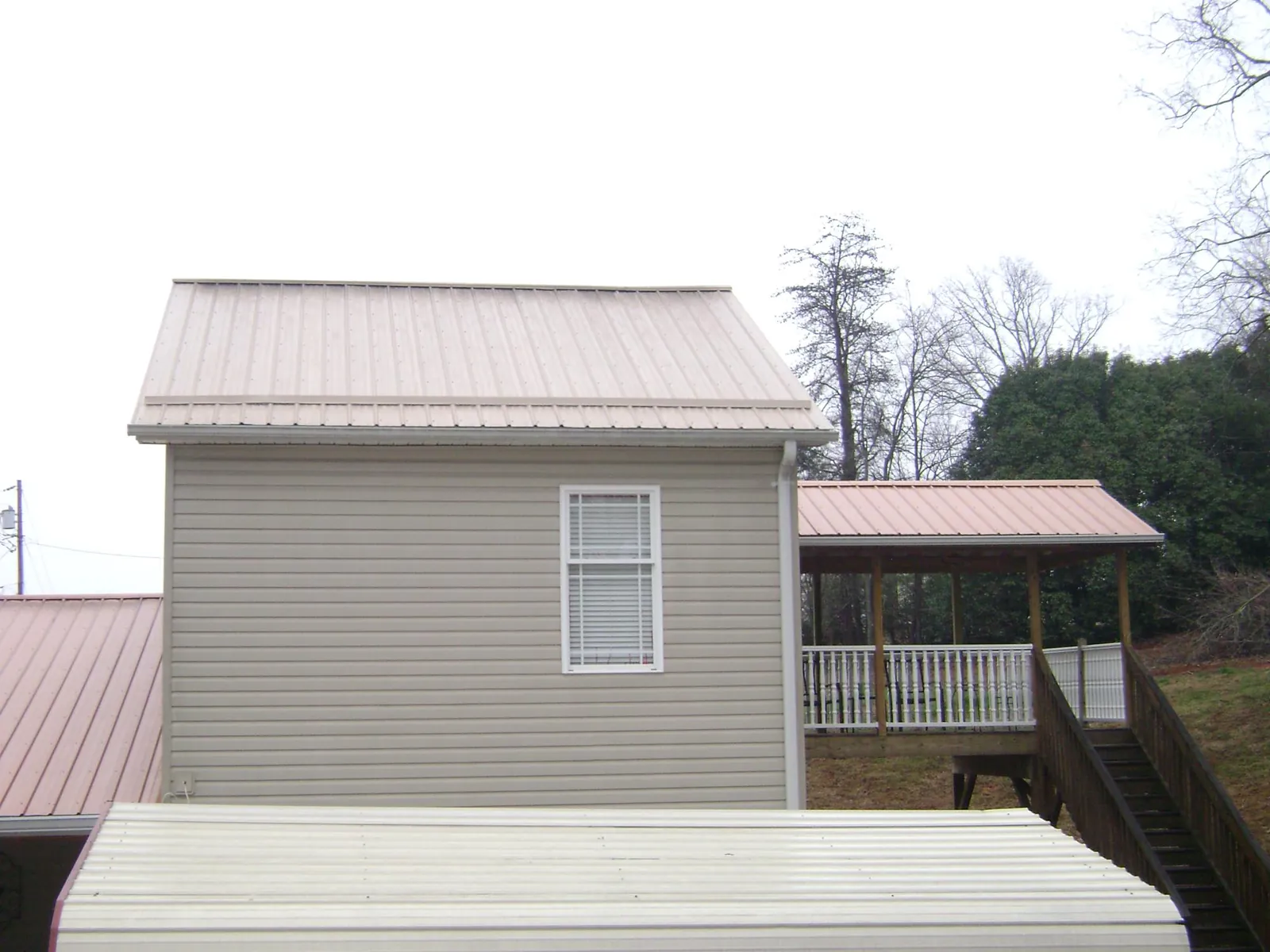 Tan metal roofs on a two story addition and attached porch, from a Roof Replacement job in Glenn